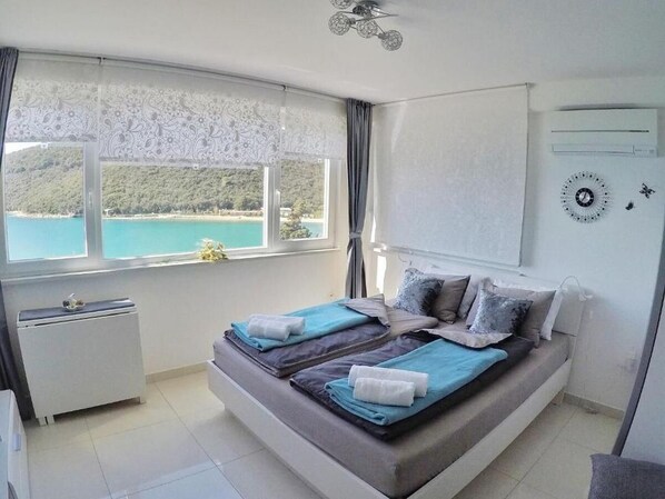 Une chambre à coucher comprenant un lit, un radiateur, une fenêtre donnant sur une plage et un climatiseur fixé au mur.
