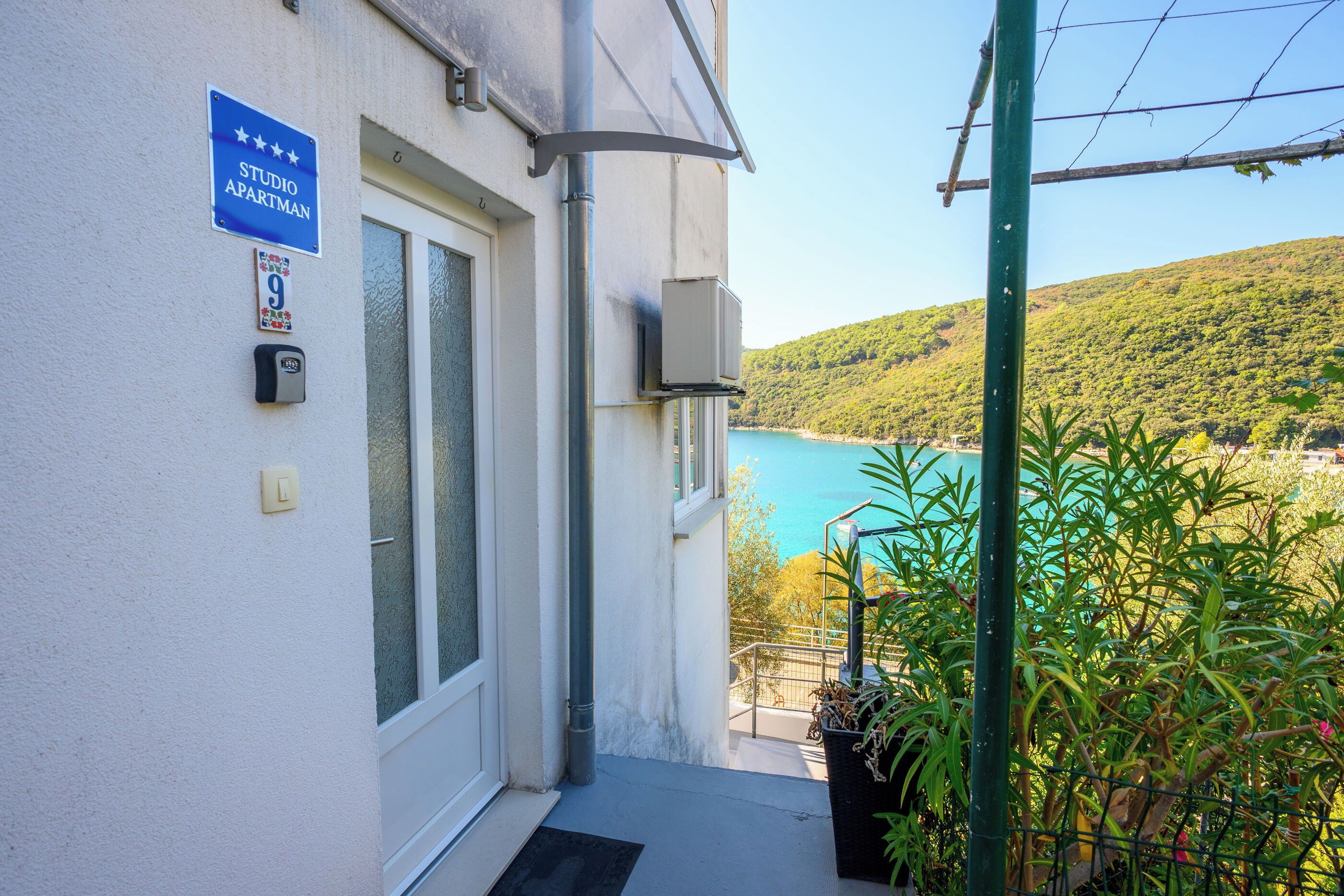 A building entrance with a sign indicating a studio apartment, a door, a mailbox, and a view of a body of water and hills.