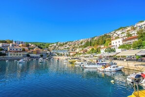 Un pueblo costero con un puerto deportivo lleno de barcos, edificios con balcones y un cielo azul despejado.
