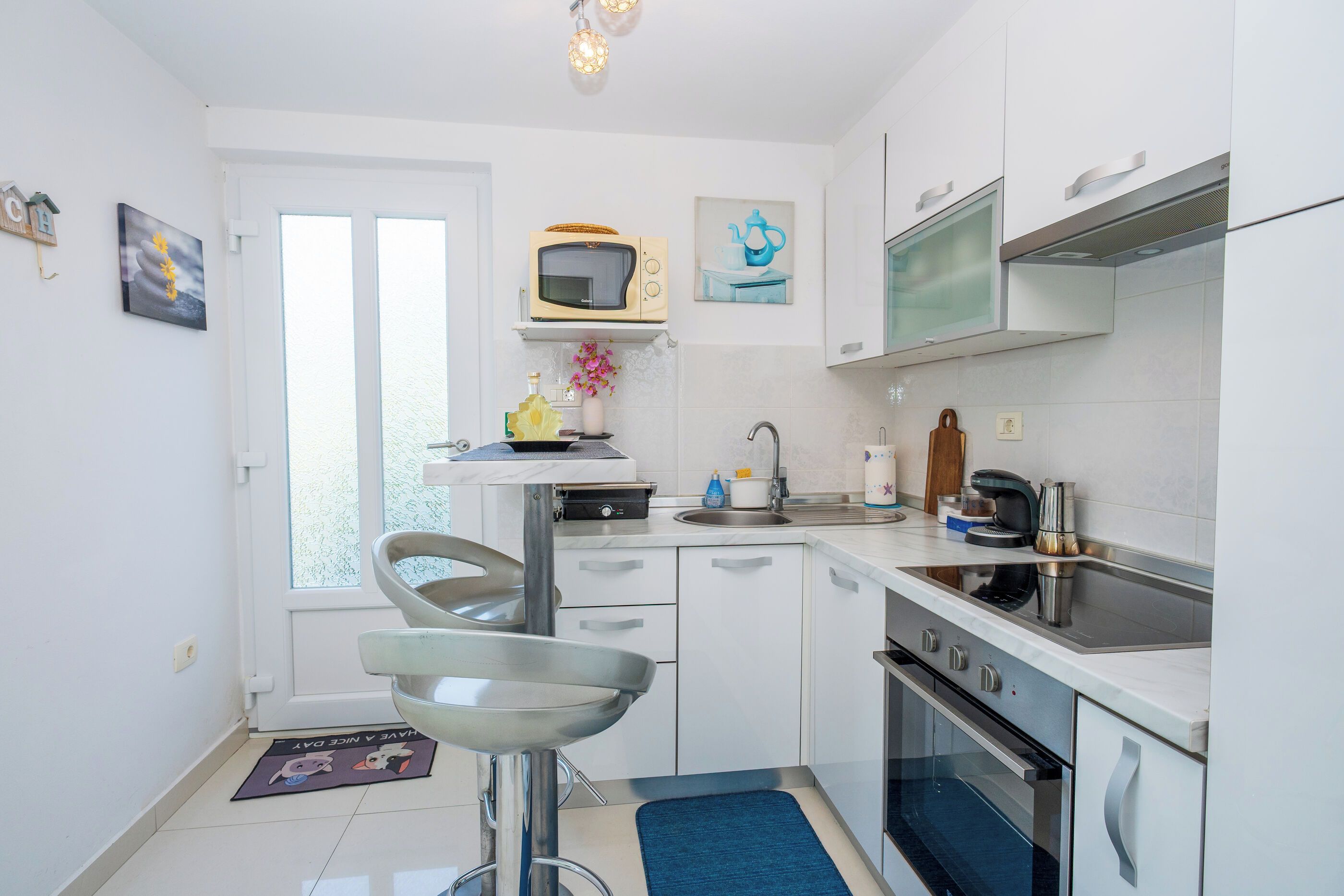 A modern kitchen with white cabinets, a microwave, a kettle, and a coffee maker.