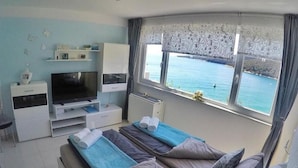 Een slaapkamer met een bed, een televisie, een bureau en uitzicht op zee.
