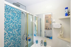 A bathroom with a shower, a sink, a mirror, and a hairdryer on a shelf. - Apartment By the Sea (Labin)
