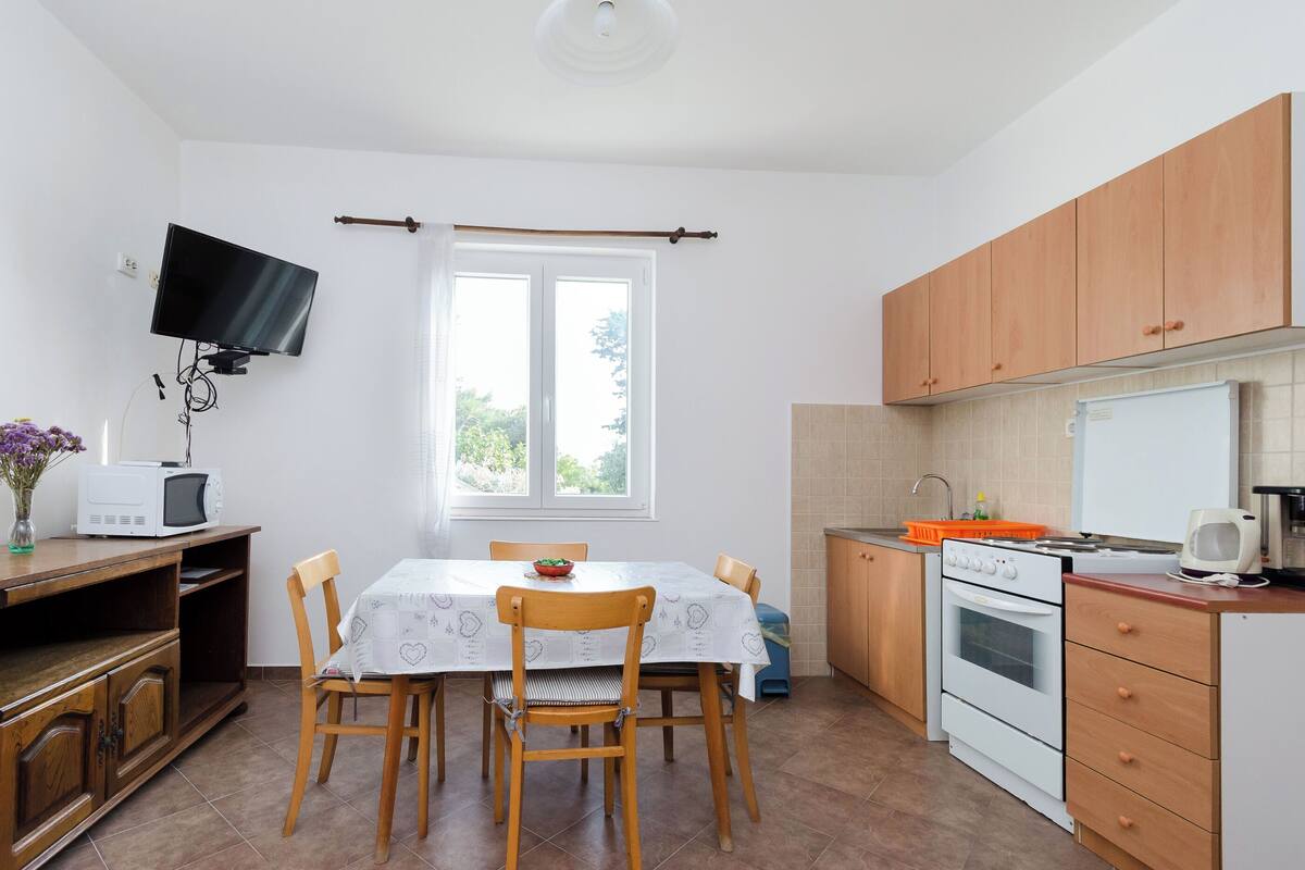 Une cuisine compacte comprenant une table à manger, des chaises, un four à micro-ondes, une cuisinière et des armoires en bois.