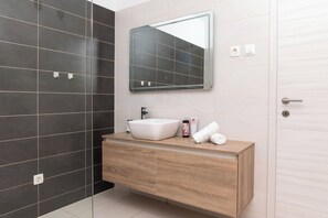 Un bagno moderno con uno specchio grande, un lavandino bianco e un mobile contenitore in legno.