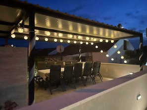 An outdoor patio with a table and chairs, string lights overhead, and a satellite dish. - Apartments Ideal Holiday (Tribunj)