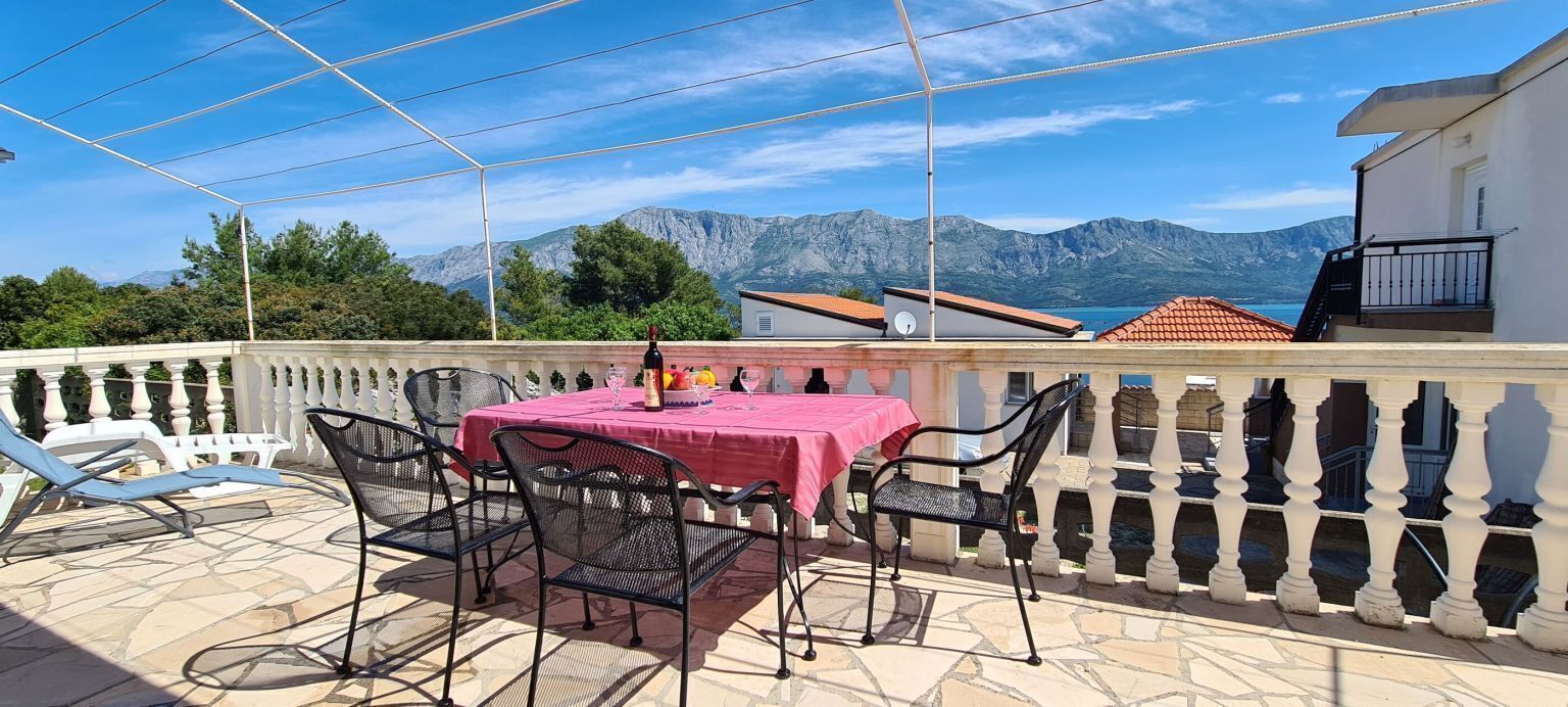Una terraza con una mesa y sillas, vistas a las montañas y un edificio con tejado rojo.