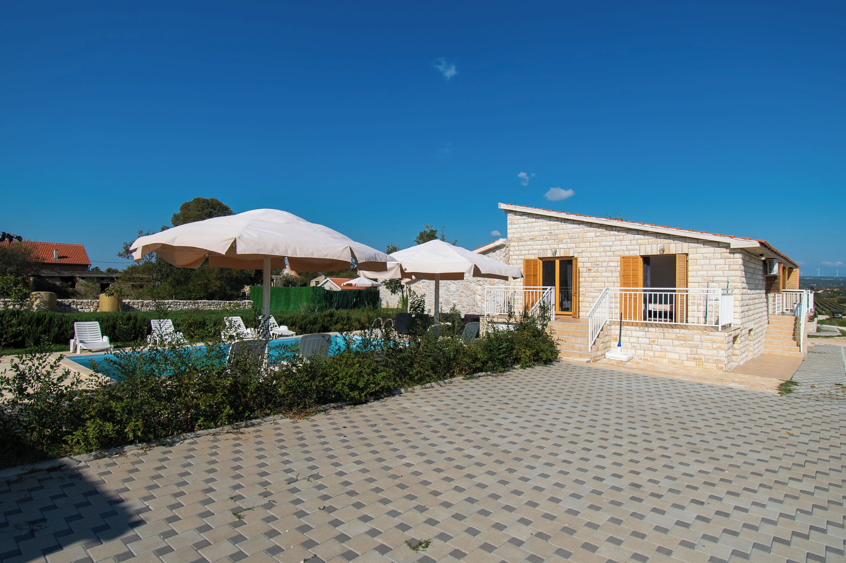 Un pequeño edificio de piedra con piscina y sombrillas.