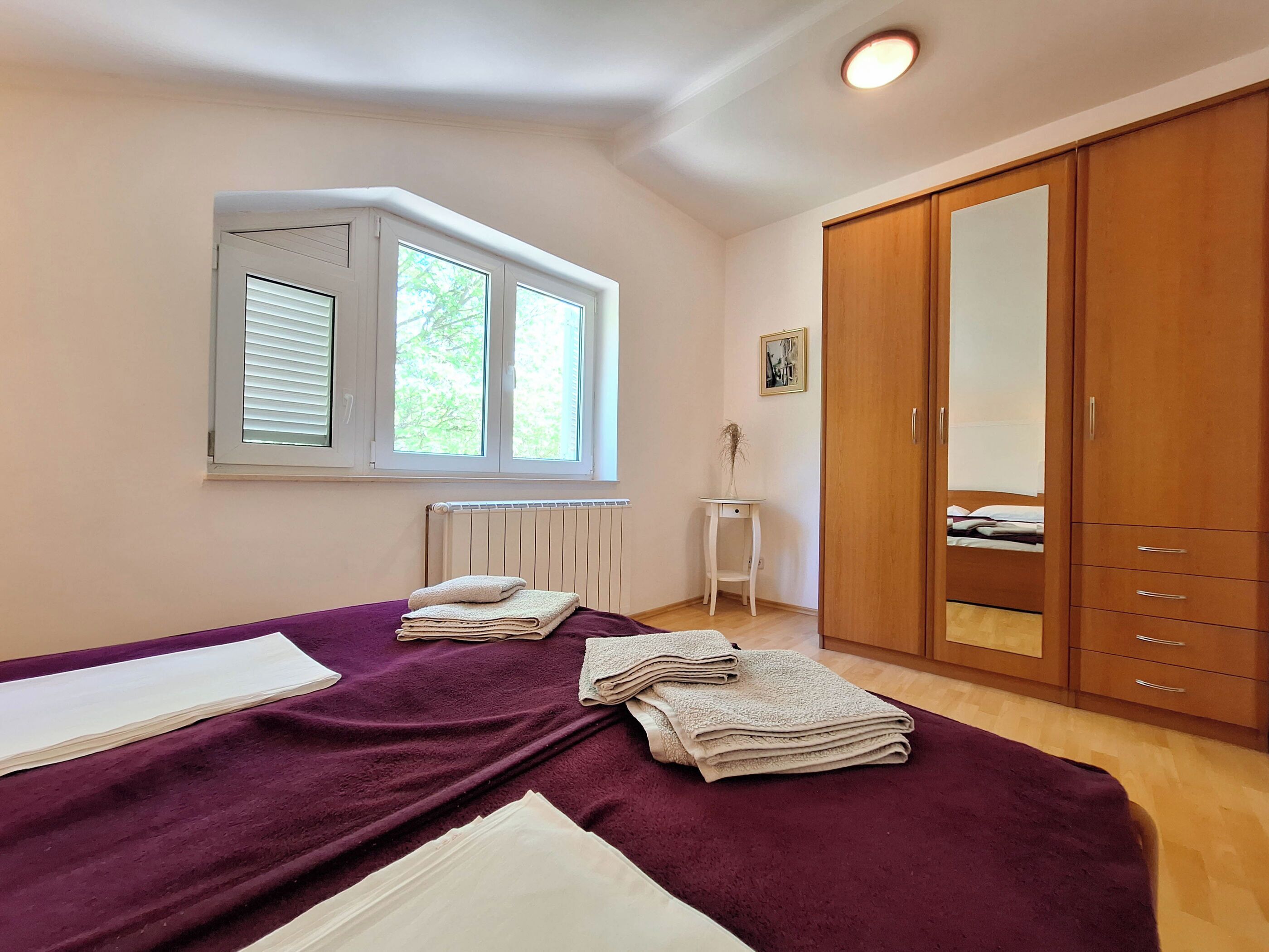 A bedroom with a bed, a wardrobe, a radiator, and a window.