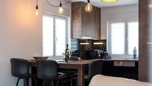 A modern kitchen with a dining area, featuring a wooden table, black chairs, and pendant lighting. - Apartment Vaya (Okrug)
