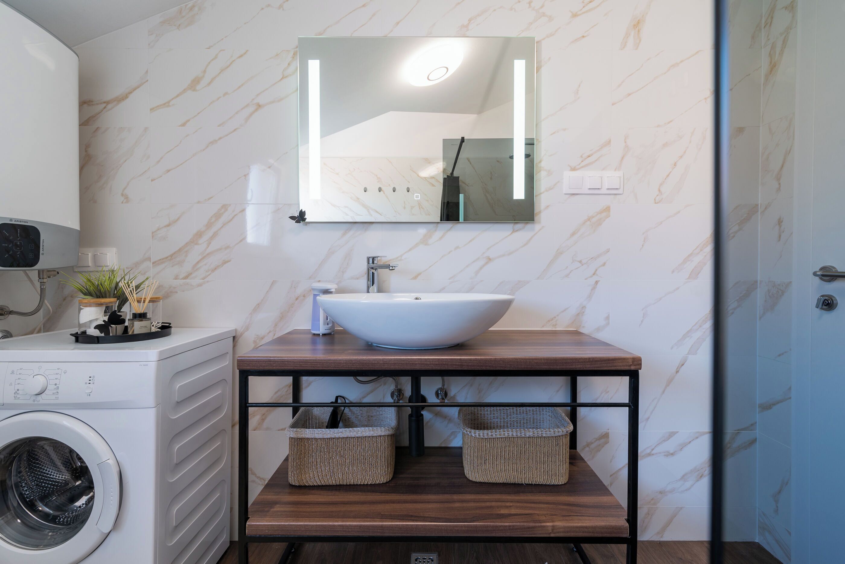 Ein modernes Badezimmer mit einem weißen Waschbecken, einer Marmor-Spritzschutzwand und einer integrierten Waschmaschine.