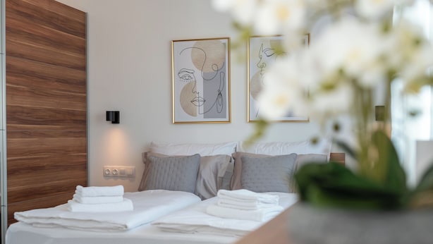 A modern bedroom with a wooden headboard, a bed with neatly folded white towels, and two abstract art pieces on the wall. - Apartment Vaya (Okrug)