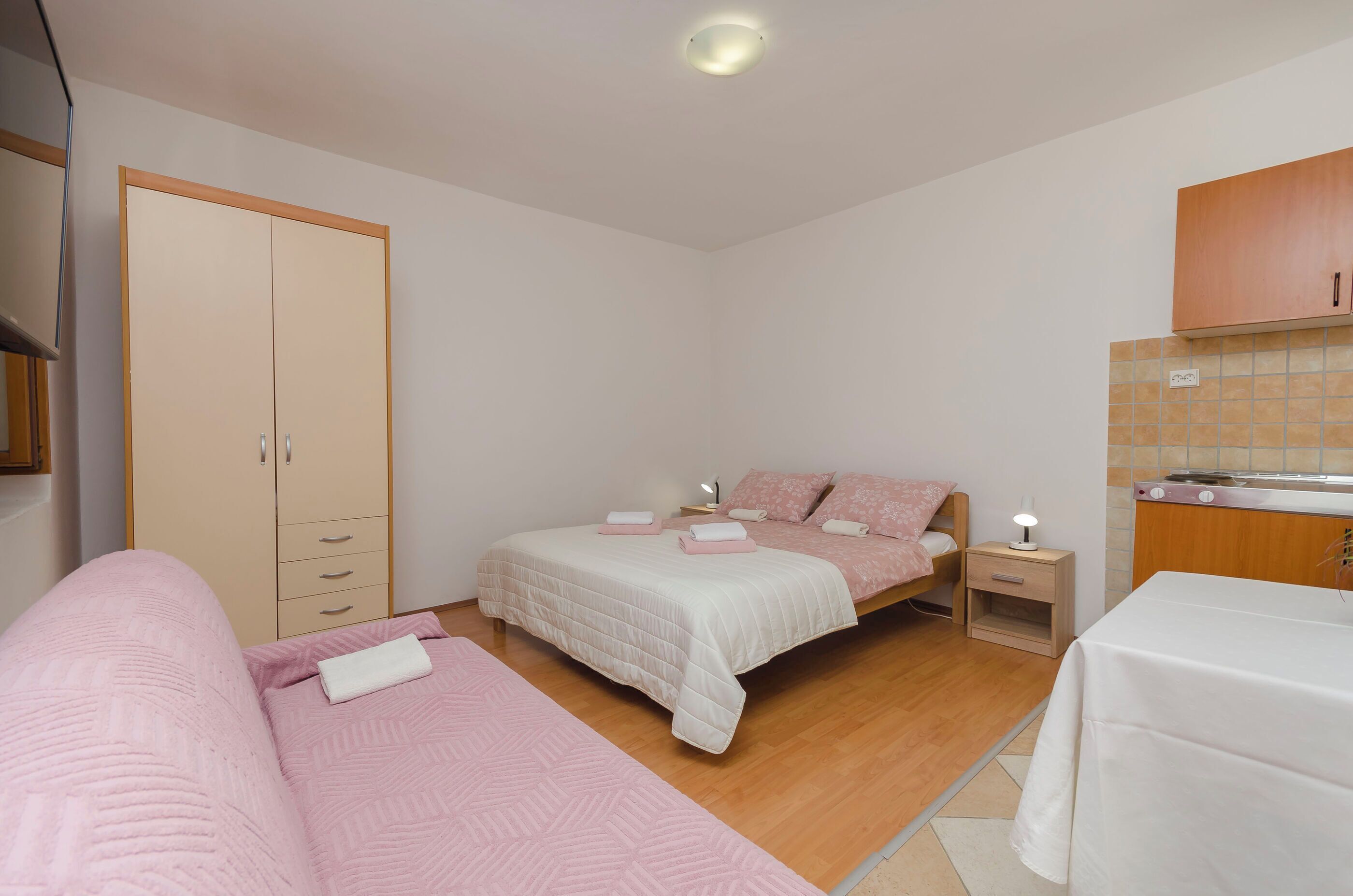 Une chambre avec deux lits, une armoire, une table de chevet avec une lampe et un petit coin cuisine.