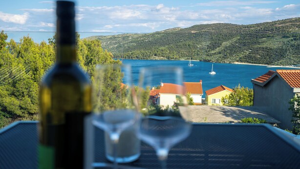 Una mesa con una botella y una copa, con vistas a un paisaje costero con casas y un cielo despejado.