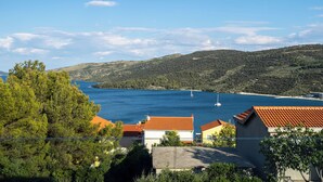 Un pueblo costero con casas de techo rojo, un mar azul cristalino y un paisaje montañoso al fondo.