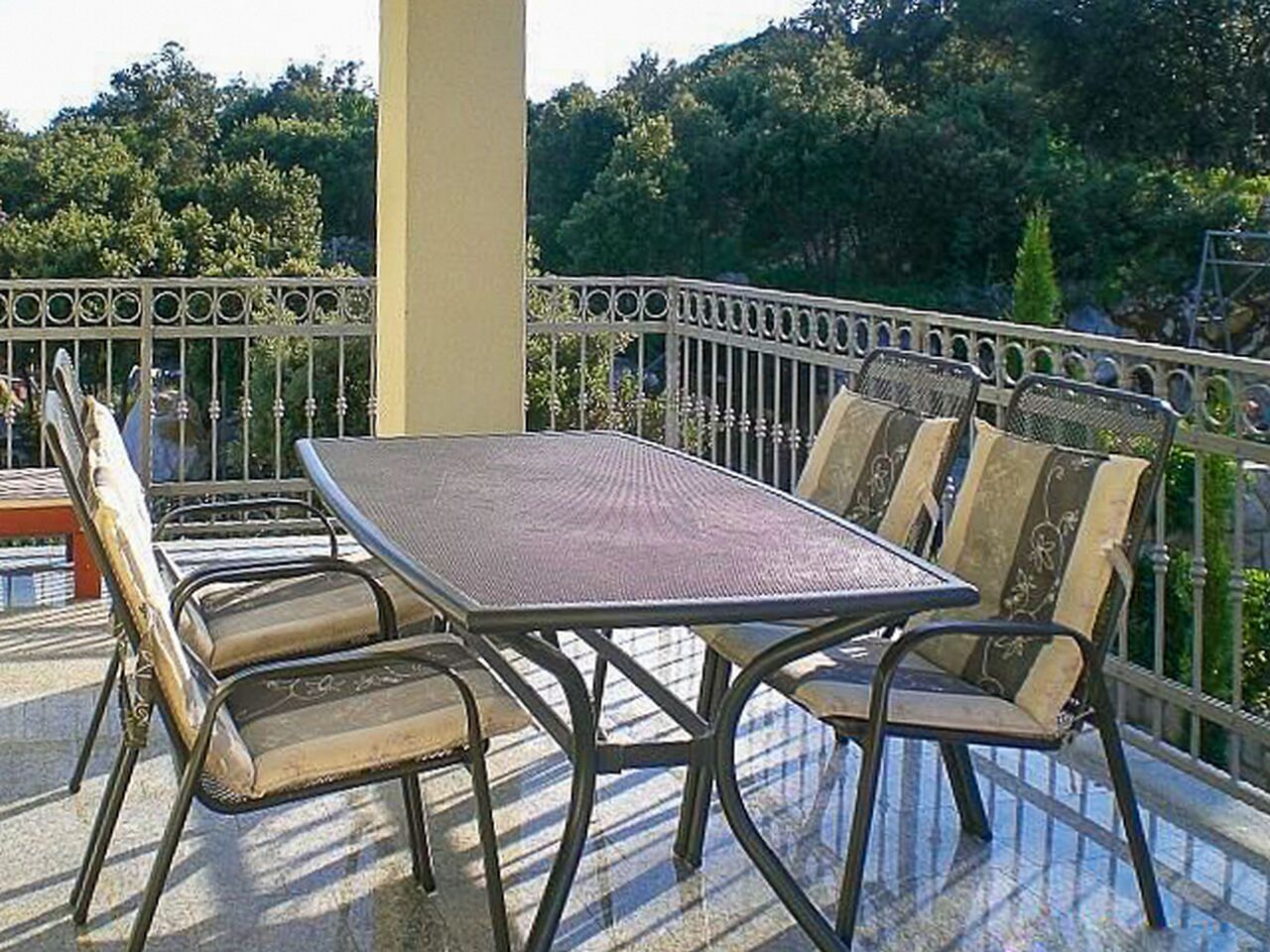 Un balcon avec une table et des chaises, entouré d’une rambarde en métal.