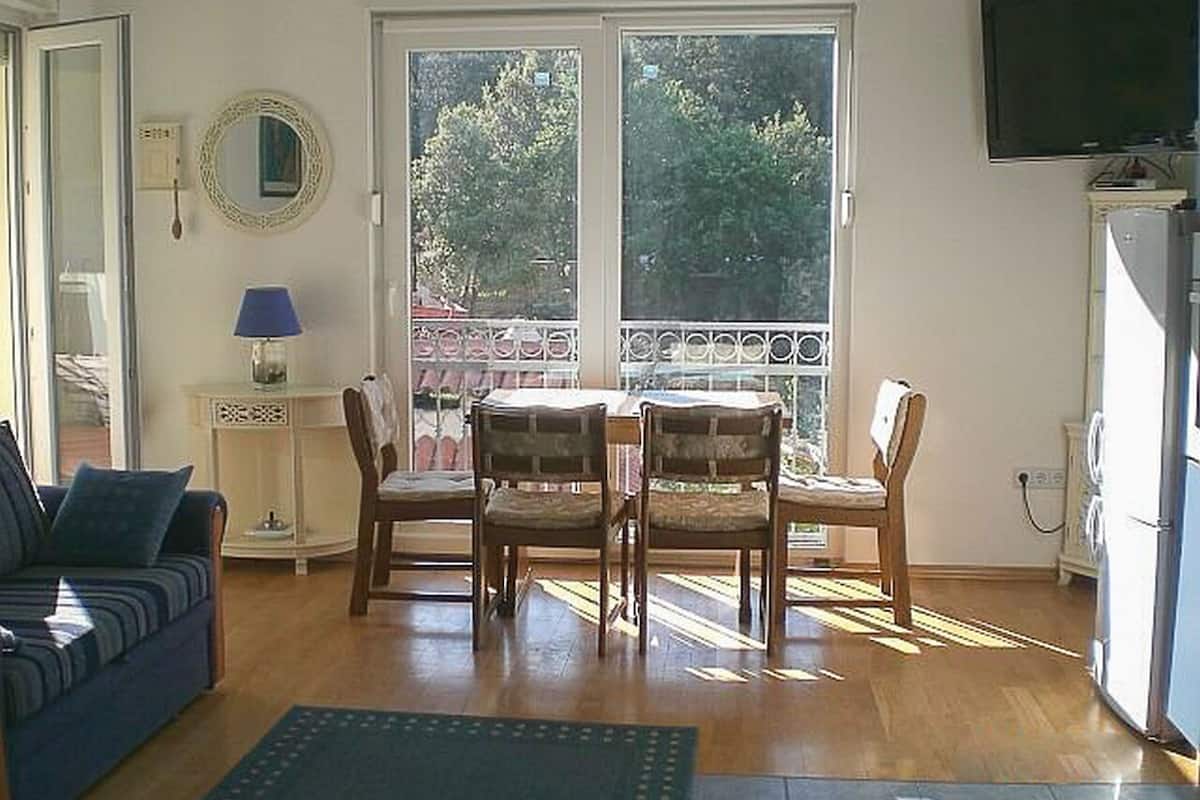 A living room with a sofa, a table with chairs, a TV, and a refrigerator.