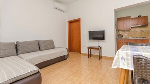 En stue med sofa, fjernsyn, et lille bord og et spiseområde med bord og stole.