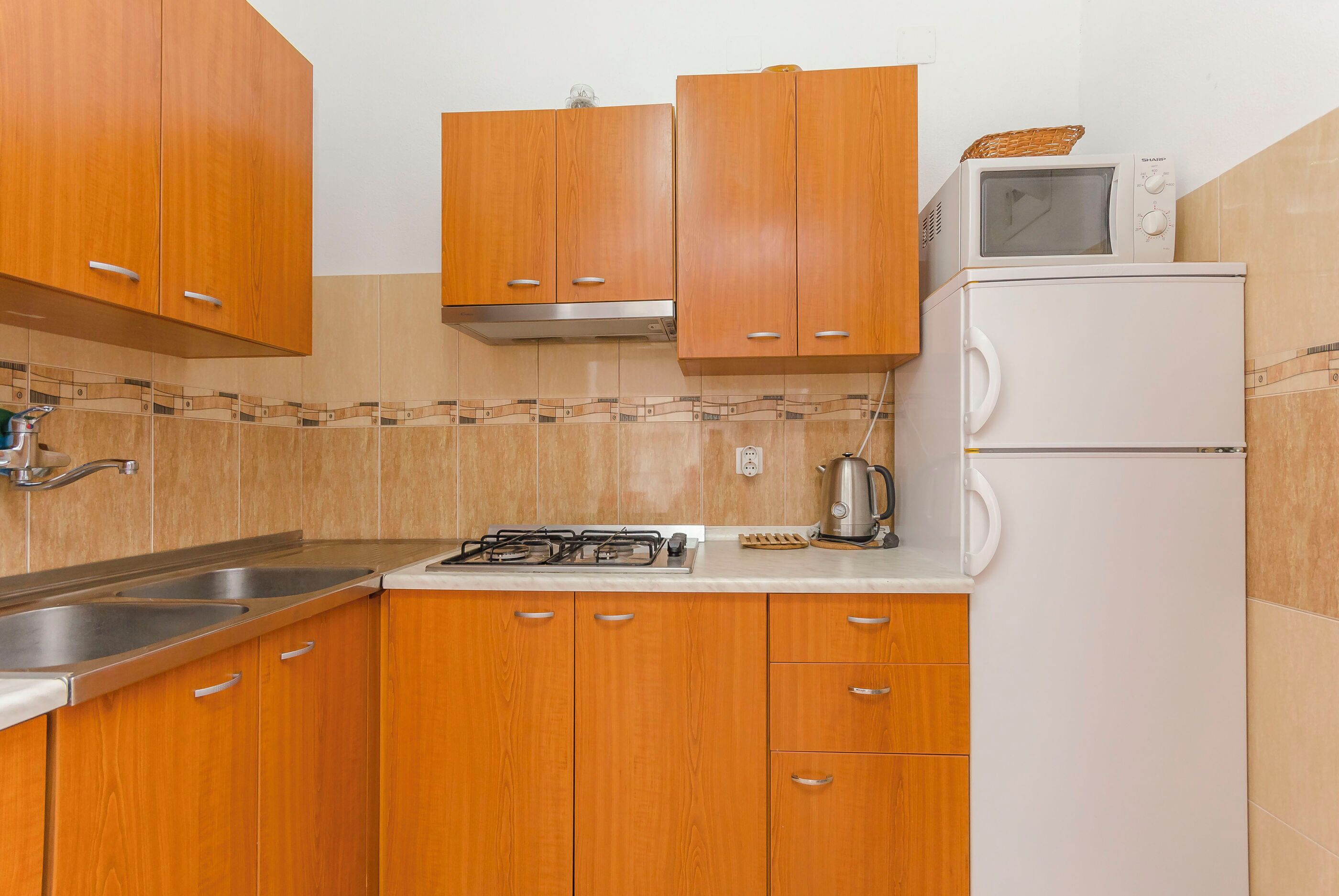 Une cuisine avec des meubles de rangement en bois, une cuisinière à gaz, un four à micro-ondes et une bouilloire.