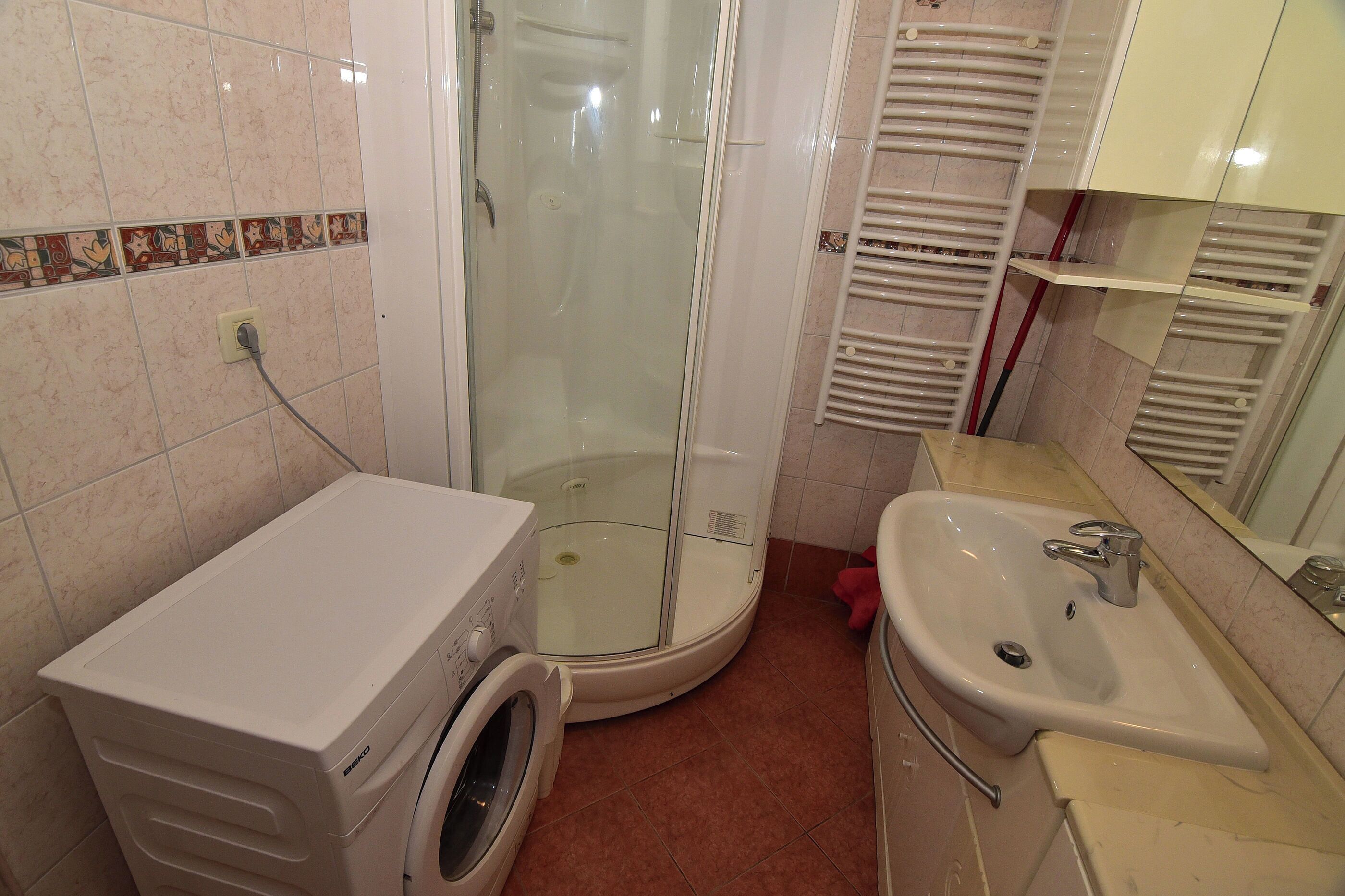 A compact bathroom with a glass-enclosed shower, a washing machine, and a sink.