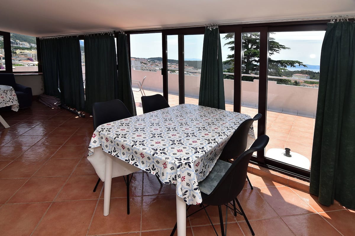 A dining area with a table and chairs, large windows with curtains, and a view of the landscape.