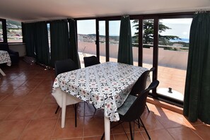 A dining area with a table and chairs, large windows with curtains, and a view of the landscape. - Apartments Good (Makarska)