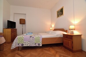 A bedroom with a bed, bedside lamps, a TV, a wooden nightstand, and a desk with a chair. - Apartments Good (Makarska)