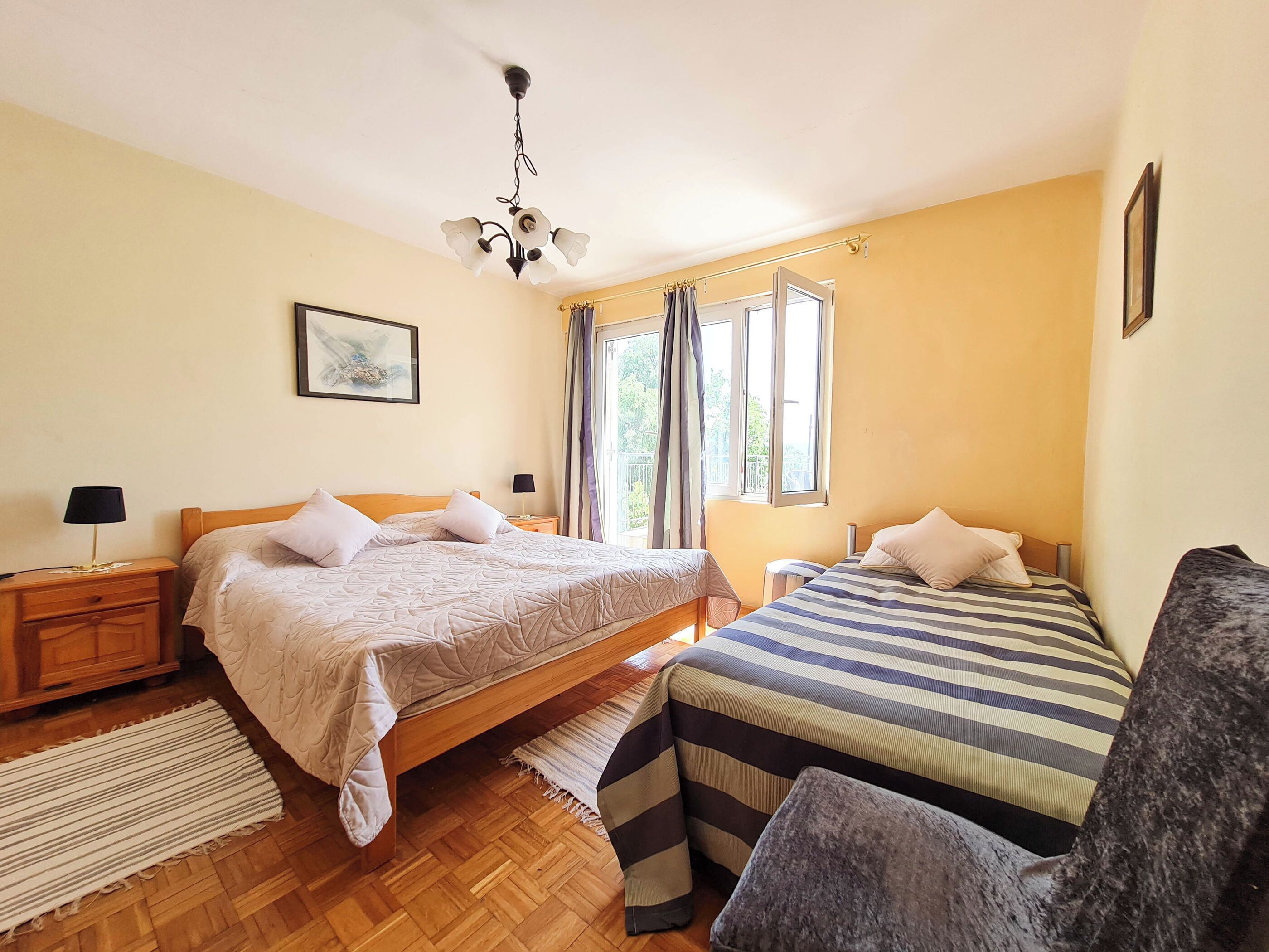 A bedroom with two beds, a wooden floor, a ceiling light fixture, and a window with curtains.