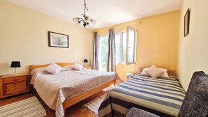 Una camera da letto con due letti, pavimento in legno, lampadario a soffitto e finestra con tende.