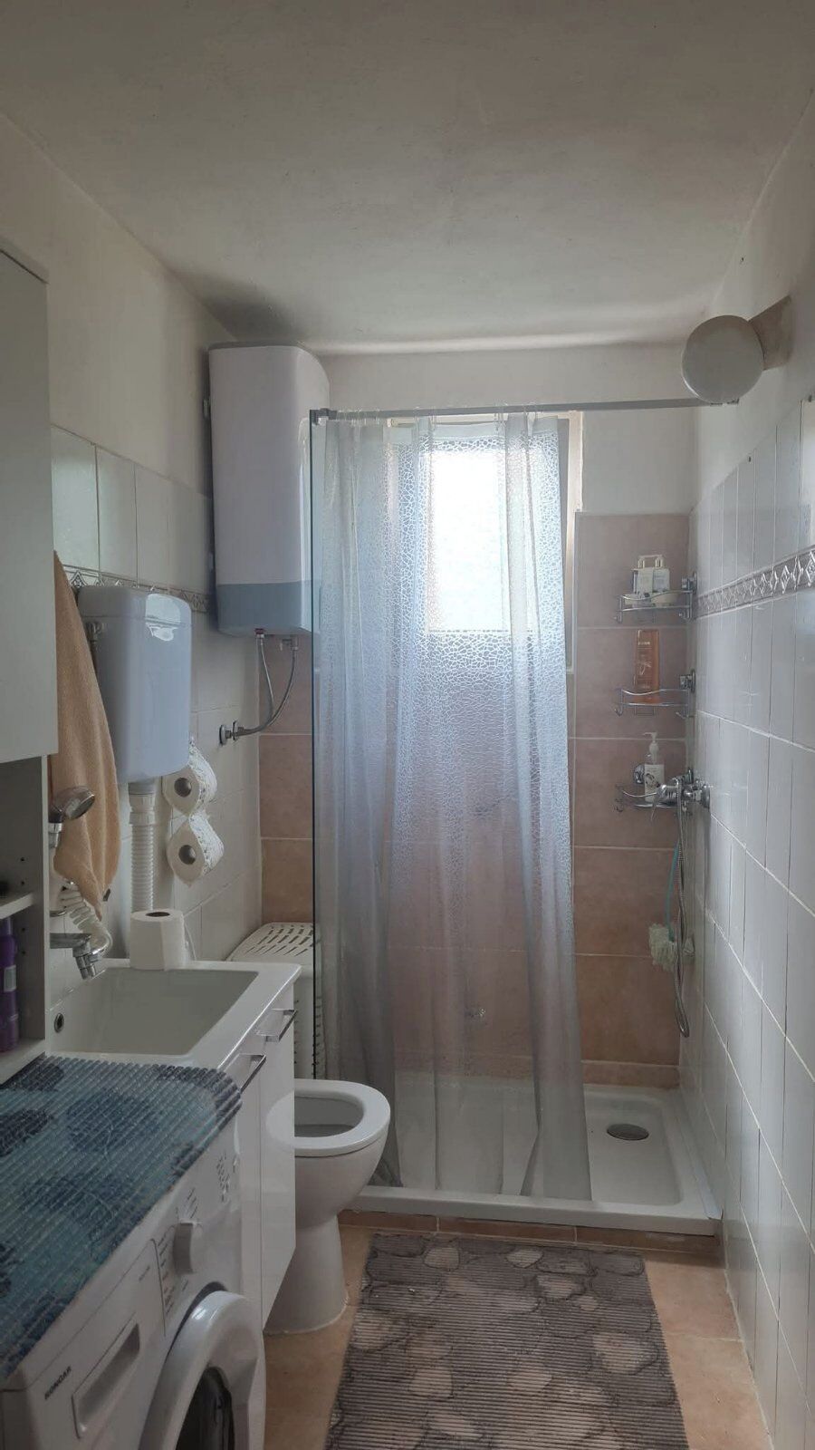 Ein kleines Badezimmer mit Dusche, Toilette und Waschmaschine.