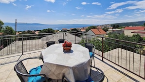 Una terrazza con tavolo e sedie, vista sulla costa, con case e montagne sullo sfondo.