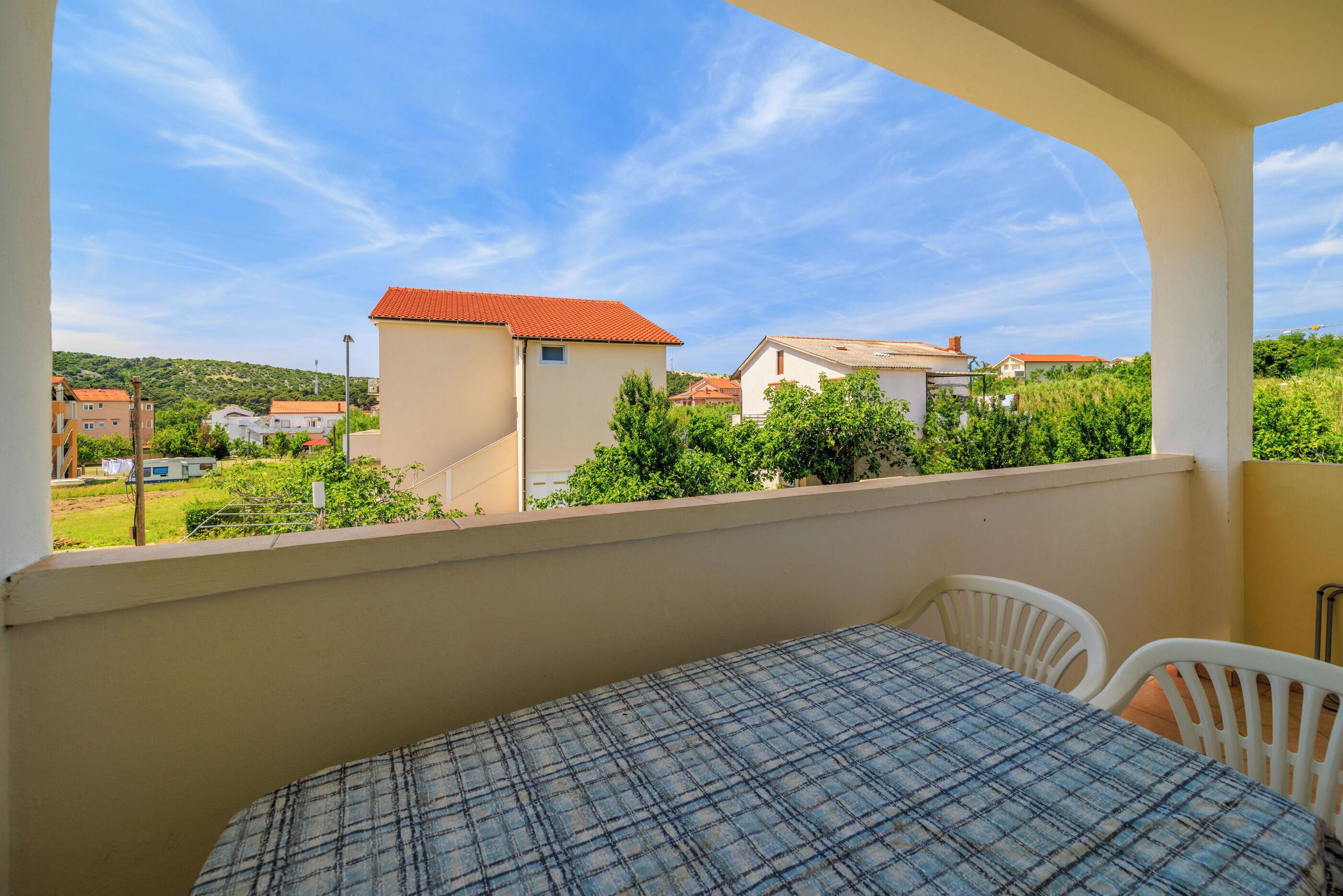 A balcony with a table and chairs, overlooking a residential area with houses and greenery.
