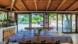 Un plafond en bois, une table recouverte d’une nappe, un banc et une vue sur l’extérieur.