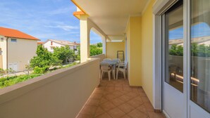 Un balcon avec une table et des chaises, une porte-fenêtre coulissante et une vue sur les maisons voisines.