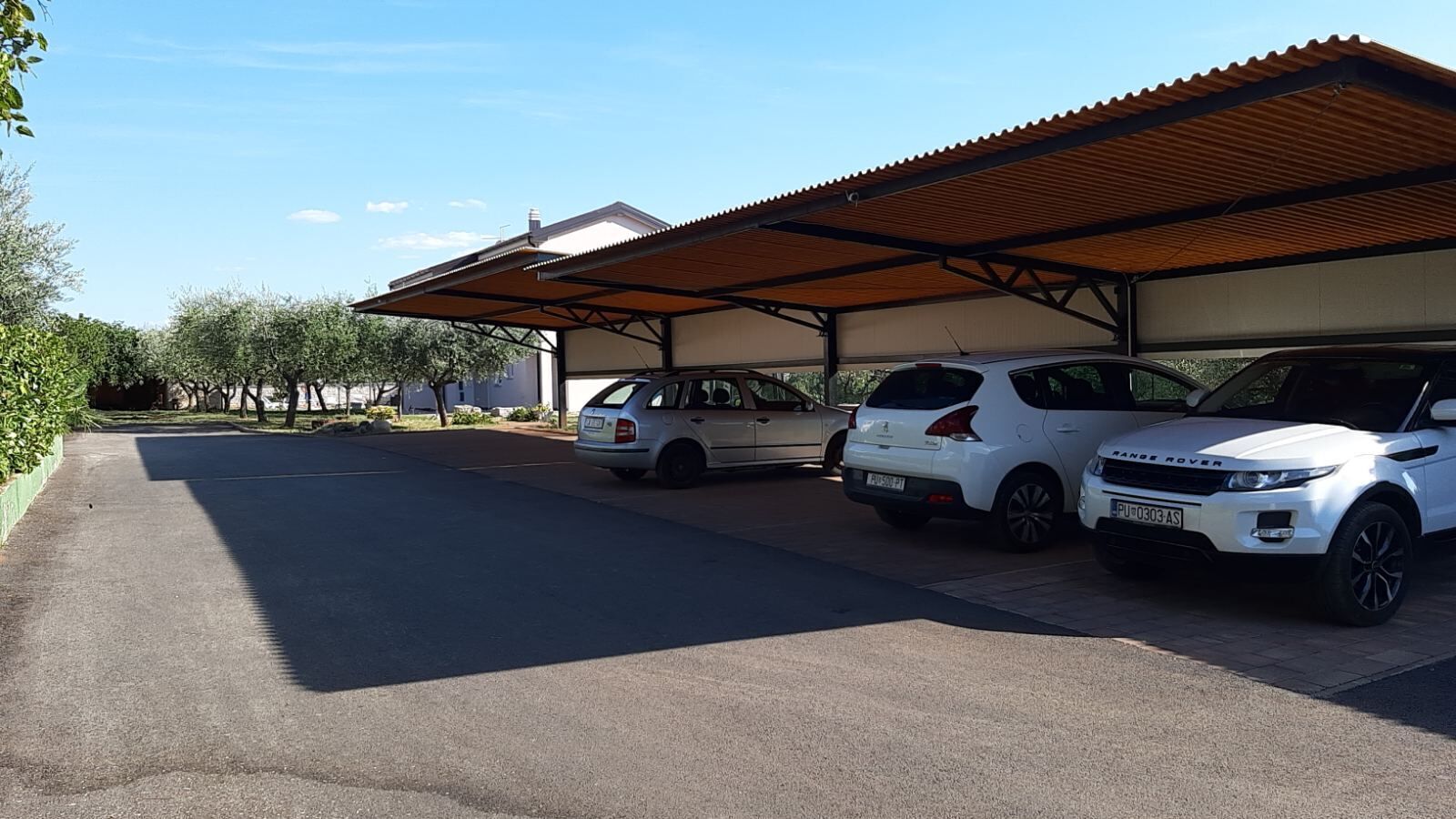 Un espace de stationnement où trois voitures blanches sont garées sous une structure abritée.