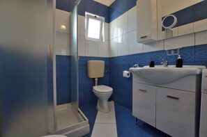 A bathroom with a shower, toilet, and sink, featuring blue and white tiles. - Apartments Emil (Umag)