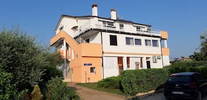 Una casa a due piani con un balcone, una scala e un'auto parcheggiata davanti.