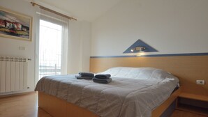 Un letto rifatto con cura, con una coperta a motivi geometrici, un comodino e una lampada a parete.
