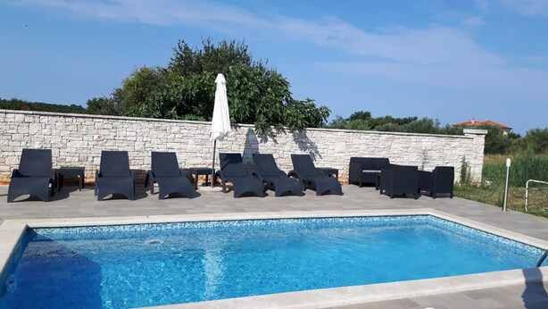 Una piscina con lettini e una parete in pietra.