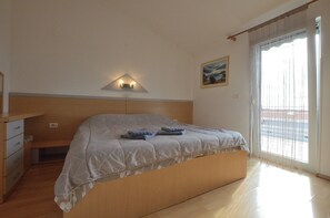 A bedroom with a bed, a bedside table, a lamp, and a window with curtains. - Apartments Emil (Umag)