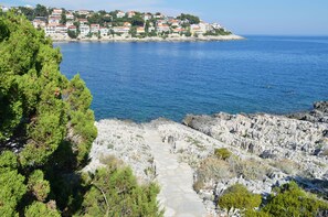 A coastal town with a rocky path leading to a beach, surrounded by greenery and buildings with red roofs. - Apartments Malo Misto (Korčula)