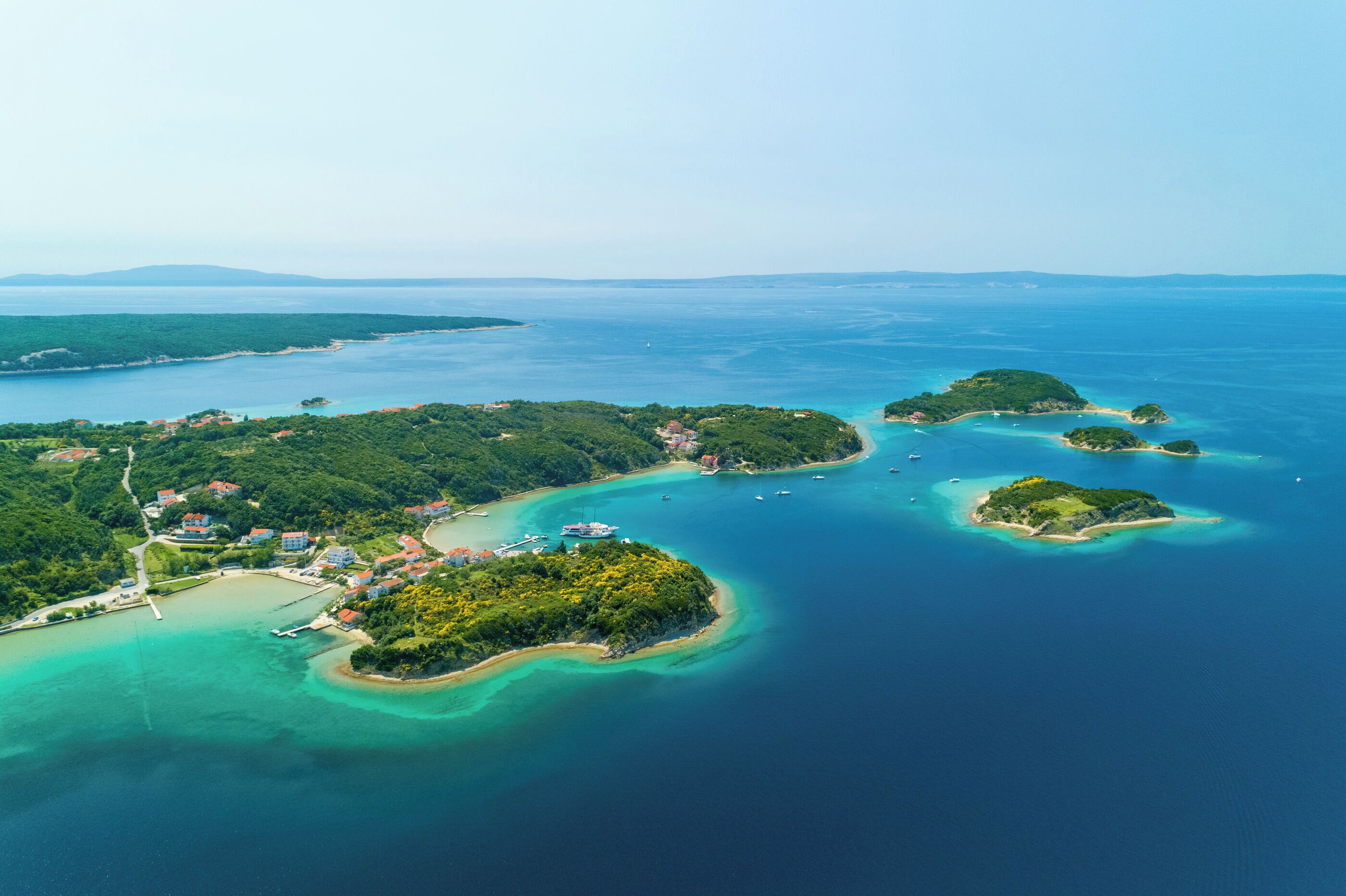 An aerial view of a coastal area with multiple islands, clear turquoise waters, and a few buildings on the largest island.