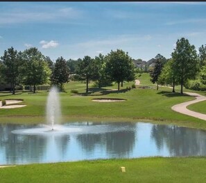 A golf course with a pond, trees, and a clear sky.