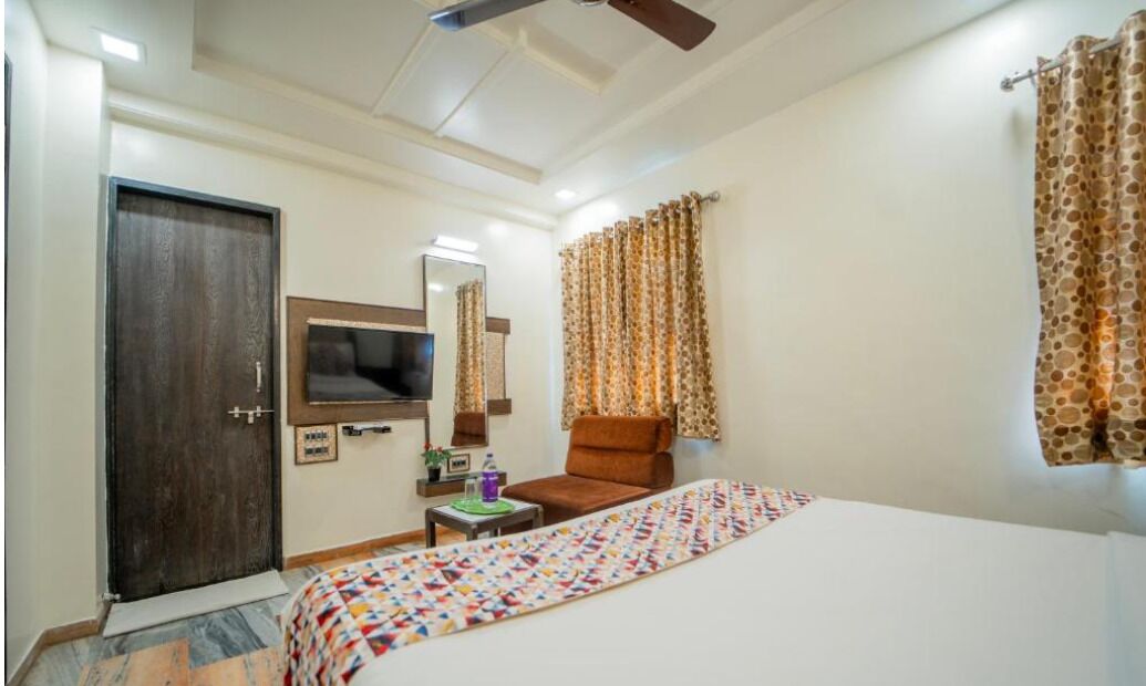 Una camera d'hotel con un letto, una sedia, una televisione, un ventilatore a soffitto e tende.