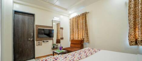 Una camera d'hotel con un letto, una sedia, una televisione, un ventilatore a soffitto e tende.