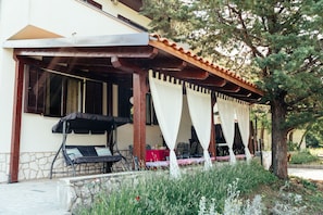 Un área de estar al aire libre con techo, pared de piedra, pérgola y un árbol.