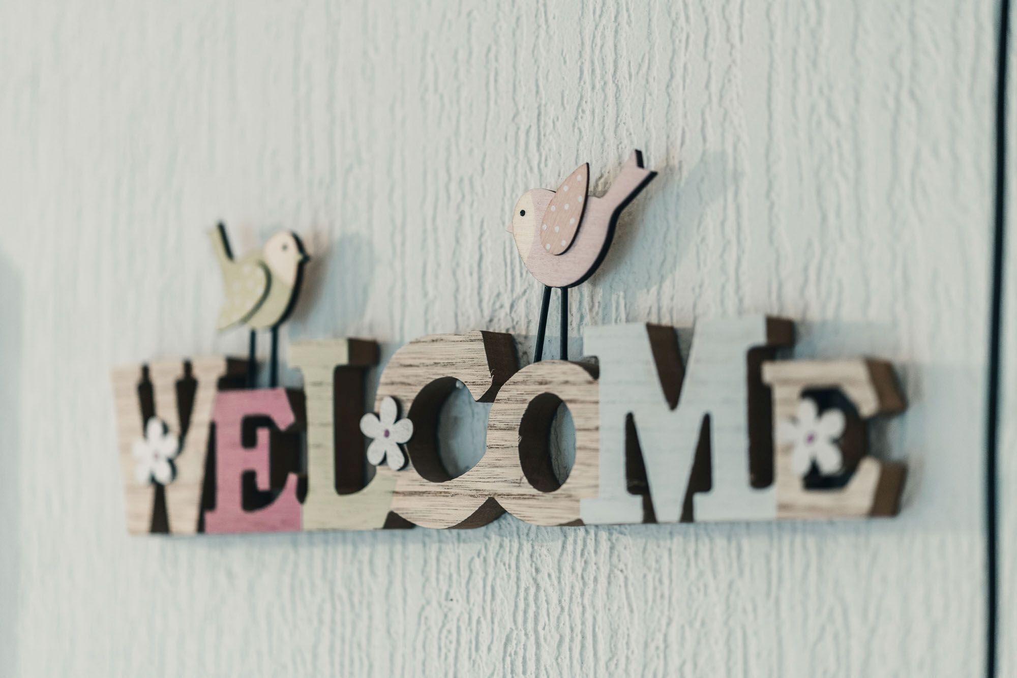 Ein hölzernes Schild mit der Aufschrift "WELCOME" und dekorativen Vogelmotiven.