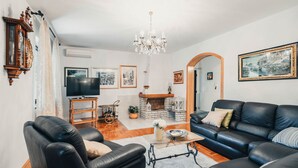 A living room with a black leather sofa, a TV, a chandelier, and a fireplace. - Apartment Peaceful Paradise (Bakar)