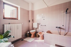 Ein Badezimmer mit Toilette, Bidet und Badewanne, alles in einem hellrosa Farbschema.