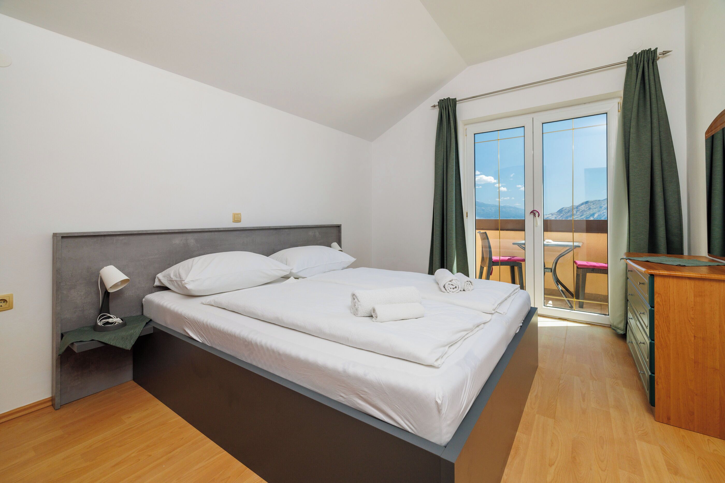 A modern bedroom with a bed, a nightstand, a desk, and a view of the outdoors.