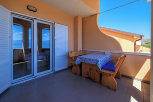 En balkon med træbænk og bord, en skydedør og havudsigt.